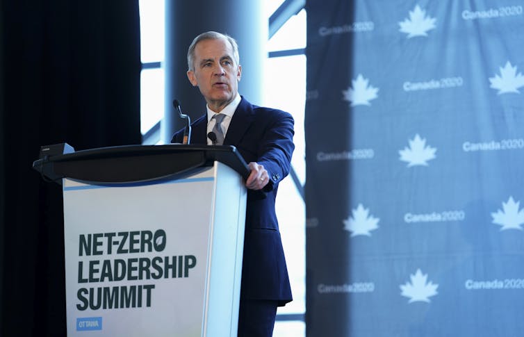 A man with short-grey hair speaks from behind a lectern that reads Net Zero Leadership Summit.